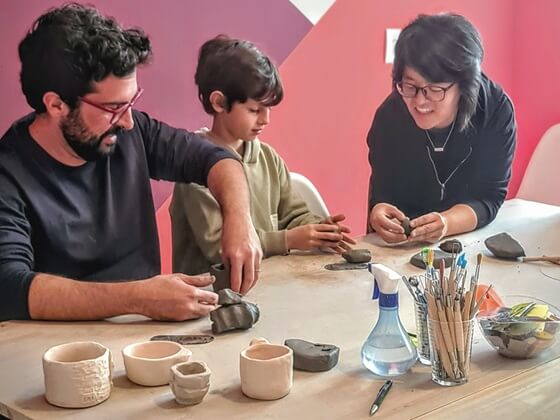 Pai e filho recebem orientação da professora Simoni Nishimura em oficina de cerâmica