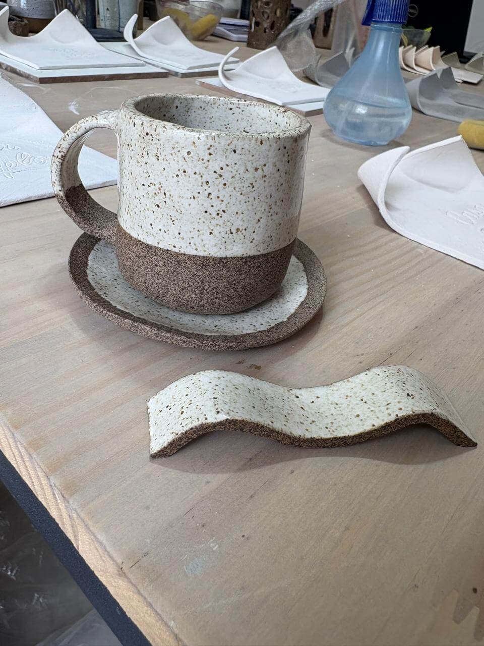 Foto de conjunto de caneca e pires, feitos em cerâmica artesanal, sobre a mesa do ateliê Shoyu Crafts.