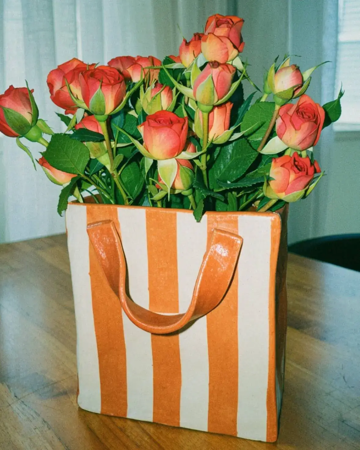 Foto de peça de cerâmica artesanal em formato de sacola de presente, com buquê de rosas dentro.