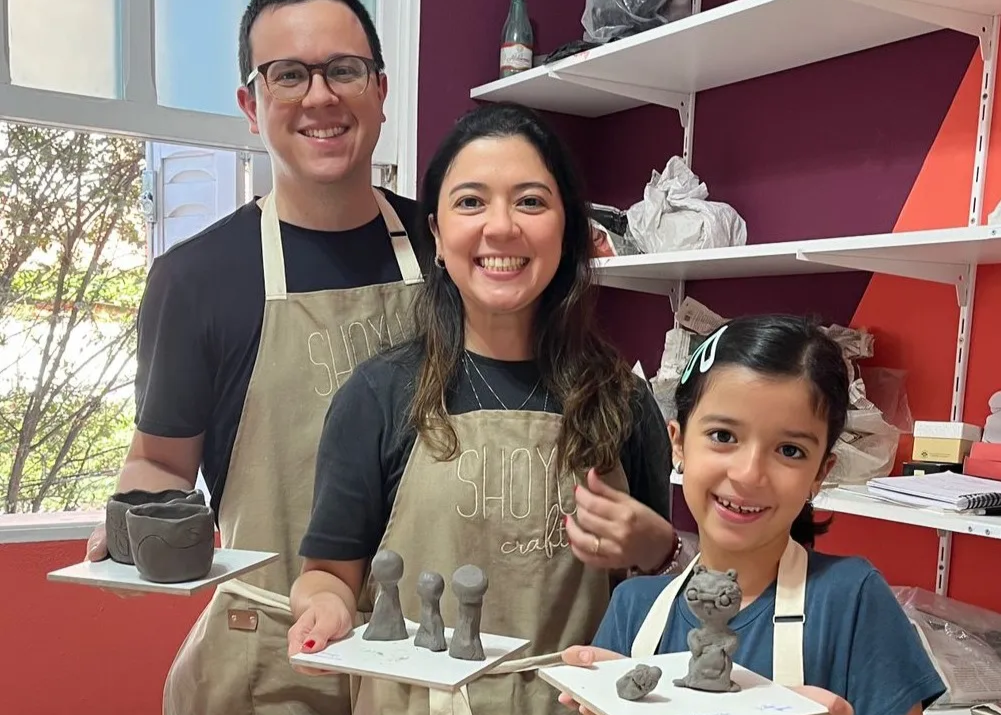 Pai, mãe e filha posam com peças modeladas em oficina familiar de cerâmica